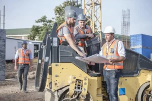 Trabajadores coordinando actividades empresariales en obra de construcción, revisando documentación CAE con equipos de protección individual