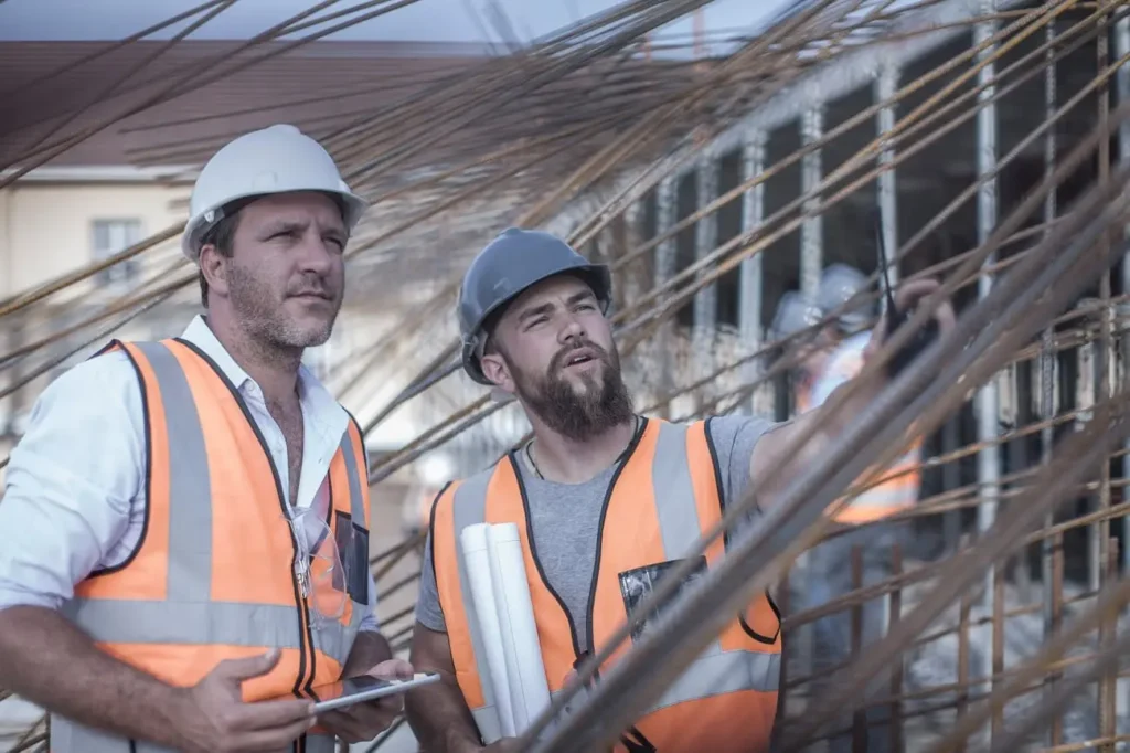 Dos profesionales con equipos de protección individual supervisando estructura en obra, ejemplo de gestión eficiente de contratistas en sector construcción