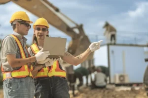 Dos técnicos de prevención con cascos y chalecos de seguridad revisando riesgos laborales en obra con contratas y subcontratas