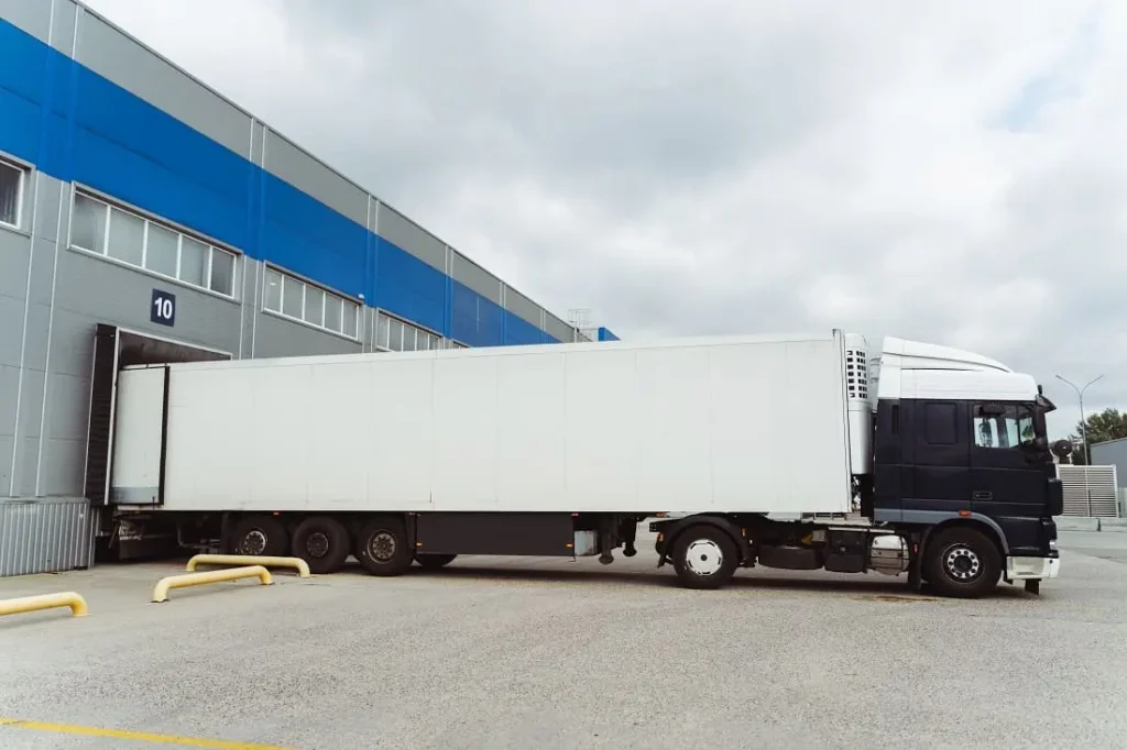 Camión refrigerado estacionado en muelle de carga de centro logístico, mostrando operaciones de transporte donde se aplican medidas de prevención de riesgos laborales en el sector logístico