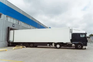 Camión refrigerado estacionado en muelle de carga de centro logístico, mostrando operaciones de transporte donde se aplican medidas de prevención de riesgos laborales en el sector logístico