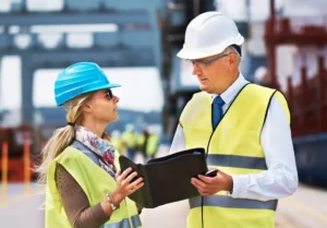 Delegado de prevención supervisando trabajo en fábrica con casco y chaleco, representando vigilancia de seguridad laboral según Ley 31/1995
