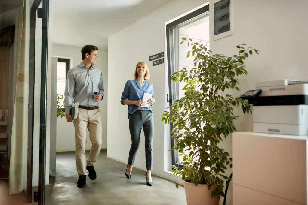 Dos compañeros de trabajo caminando juntos por el pasillo de una oficina durante un proceso de reincorporación tras baja de larga duración