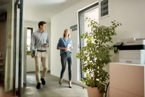 Dos compañeros de trabajo caminando juntos por el pasillo de una oficina durante un proceso de reincorporación tras baja de larga duración