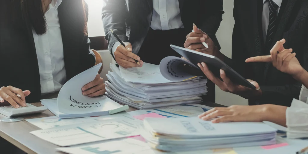 Equipo de profesionales revisando pilas de documentos en papel sobre una mesa de trabajo, representando la gestión manual de permisos de trabajo