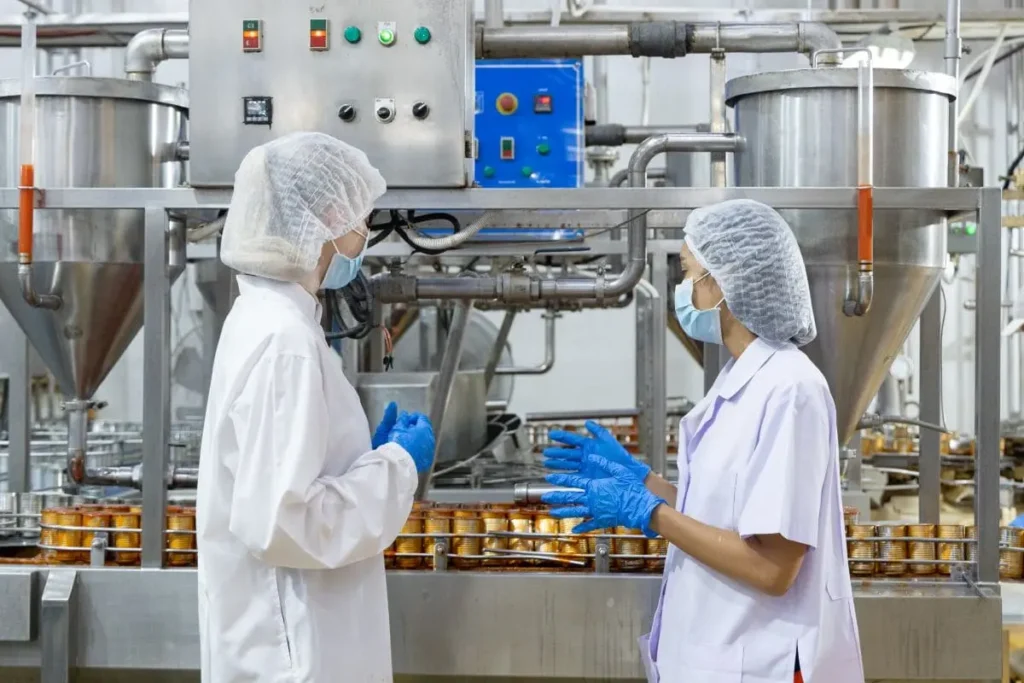 Dos trabajadoras con EPI en planta de producción alimentaria gestionando la coordinación de actividades empresariales en el sector de la alimentación
