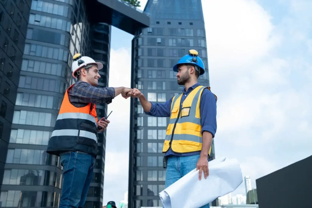 Dos trabajadores de la construcción chocando el puño frente a rascacielos, representando la coordinación segura entre empresas que facilita un software CAE con inteligencia artificial