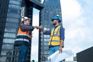Dos trabajadores de la construcción chocando el puño frente a rascacielos, representando la coordinación segura entre empresas que facilita un software CAE con inteligencia artificial