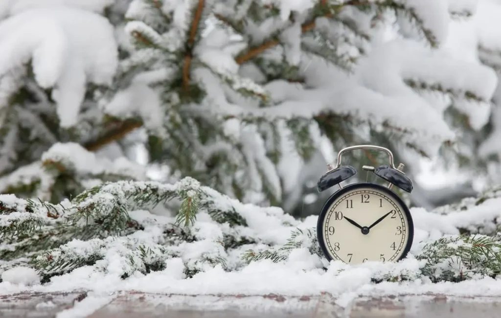 Cambio de hora y CAE - reloj despertador sobre ramas de abeto nevadas, símbolo del paso al horario de invierno