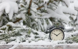 Cambio de hora y CAE - reloj despertador sobre ramas de abeto nevadas, símbolo del paso al horario de invierno
