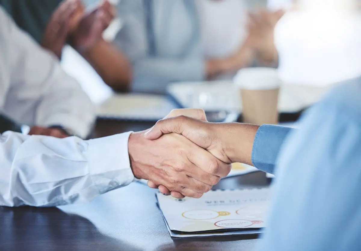 Deux professionnels se serrant la main autour d'un contrat lors d'une réunion d'affaires, illustrant la relation entre un entrepreneur principal et un sous-traitant
