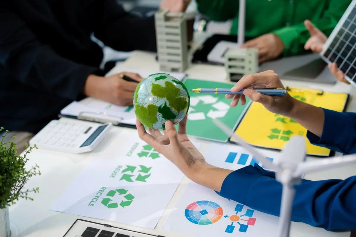 Équipe analysant des indicateurs environnementaux avec un globe et des symboles de recyclage dans le cadre de la norme ISO 14001.
