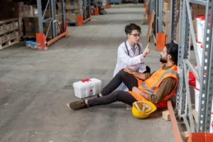Responsabile sicurezza presta primo soccorso a lavoratore appaltatore infortunato in magazzino logistico, evidenziando l'importanza della gestione proattiva della sicurezza negli appalti