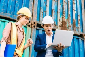 Professionisti della sicurezza sul lavoro che consultano documentazione obbligatoria in cantiere con laptop e caschi di protezione