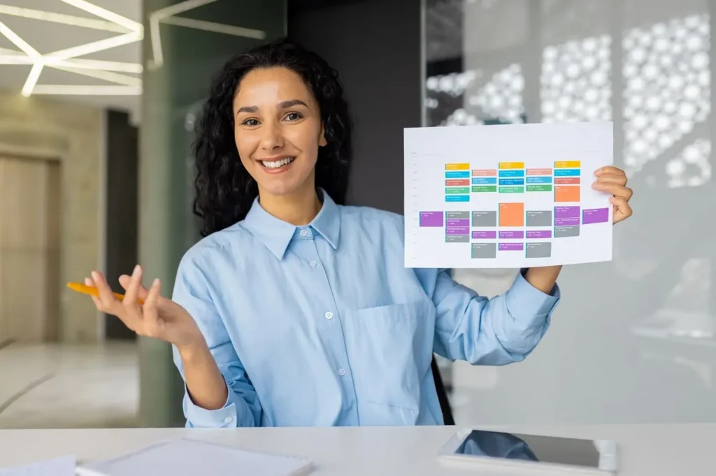 Consultora sonriente en camisa azul mostrando un diagrama de análisis en una oficina moderna con iluminación natural. La imagen transmite profesionalismo y experiencia en metodologías de resolución de problemas.